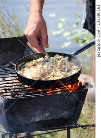 Cooking fried mussels in frying pan. Frying fresh mussels and onions near river 138596161