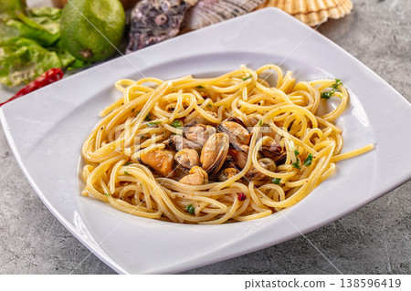 Spaghetti with mussels and herbs on a white plate with fresh seafood ingredients on a grey table Spaghetti with mussels and herbs on a white plate with fresh seafood ingredients on a grey table 138596419