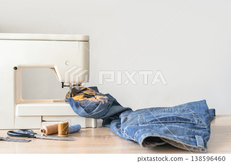Sewing machine working on heavy denim, preparing a garment. Crafting and tailoring hobby at home atelier Sewing machine working on heavy denim, preparing a garment. Crafting and tailoring hobby at home atelier 138596460
