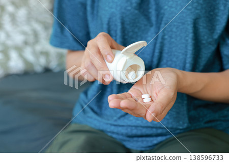 Close up of woman hands pouring white pills from a plastic bottle into her palm. Taking daily medicine, vitamin, painkiller or dietary supplement for medical healthcare and treatment concept. Close up of woman hands pouring white pills from a plastic bottle into her palm. Taking daily medicine, vitamin, painkiller or dietary supplement for medical healthcare and treatment concept. 138596733