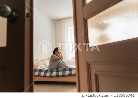 An adult woman sitting on bed with head in hands, struggling with sadness, grief, and mental health issues. Feeling lonely and isolated 138596741