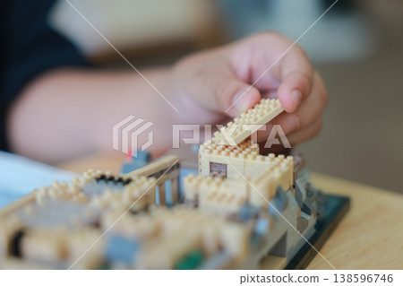 Close up of child hand assembling micro building blocks with instruction manual on wooden table. Little boy playing educational toy. Kids development, creativity, concentration and learning concept. Close up of child hand assembling micro building blocks with instruction manual on wooden table. Little boy playing educational toy. Kids development, creativity, concentration and learning concept. 138596746