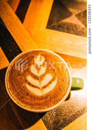 Latte art, a coffee drink with frothed milk creating a leaf pattern, resting on a geometric wooden table. A mug of hot fresh coffee creating a cozy atmosphere Latte art, a coffee drink with frothed milk creating a leaf pattern, resting on a geometric wooden table. A mug of hot fresh coffee creating a cozy atmosphere 138596945