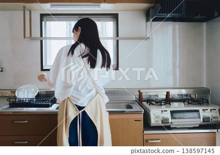 A woman putting on an apron in the kitchen; a scene from everyday life involving housework and cooking. A woman putting on an apron in the kitchen; a scene from everyday life involving housework and cooking. 138597145