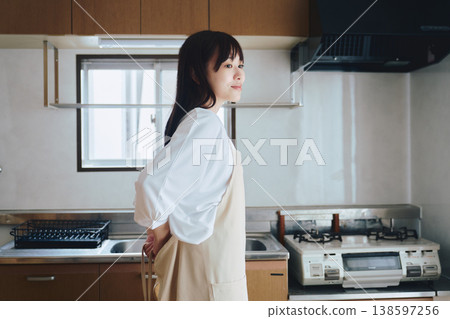 A woman putting on an apron in the kitchen; a scene of preparation before cooking. A woman putting on an apron in the kitchen; a scene of preparation before cooking. 138597256