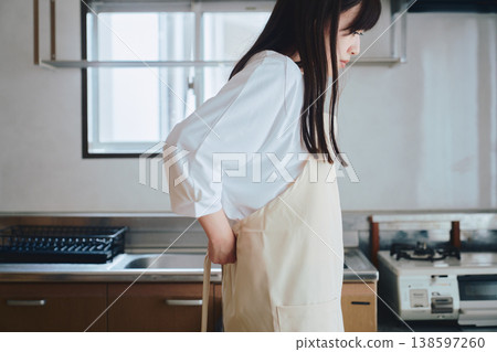 一位女士在廚房裡繫著圍裙;這是烹飪前的準備場景。 一位女士在廚房裡繫著圍裙;這是烹飪前的準備場景。 138597260