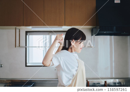 A woman putting on an apron in the kitchen; a scene of preparation before cooking. A woman putting on an apron in the kitchen; a scene of preparation before cooking. 138597261