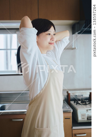一位女士在廚房裡繫著圍裙;這是烹飪前的準備場景。 一位女士在廚房裡繫著圍裙;這是烹飪前的準備場景。 138597264