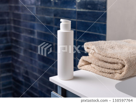 White pump cosmetic bottle near beige towel in dark blue bathroom close up, cosmetic mockup 138597764