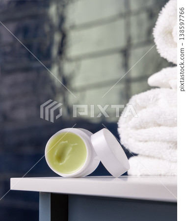 Opened handmade lip balm jar in blue bathroom with towel. Blank lid cosmetic mockup 138597766