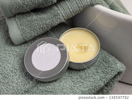 Opened cosmetic lip balm tin with metal lid with round blank label mockup on sage green bath towel 138597782