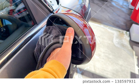 Man wiping and drying car with grey microfiber rag outdoors, closeup 138597931