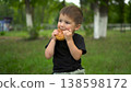 Three year old boy eats cheeseburger outdoors and looks at camera portrait 4k 138598172
