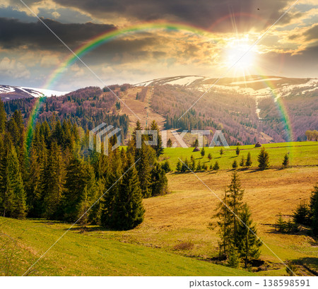 sunset over mountain landscape during spring. peaceful countryside scenery with coniferous forest near grassy field. beautiful ridge with snow capped top in the distance under the rainbow sunset over mountain landscape during spring. peaceful countryside scenery with coniferous forest near grassy field. beautiful ridge with snow capped top in the distance under the rainbow 138598591