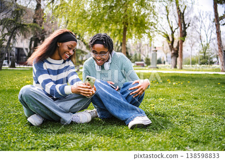 Teenagers laughing and bonding while using smartphone in park 138598833