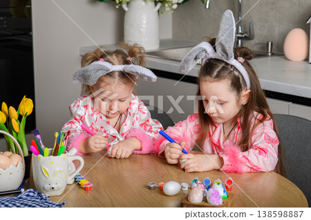 Two girls painting Easter eggs at table in kitchen Two girls painting Easter eggs at table in kitchen 138598887
