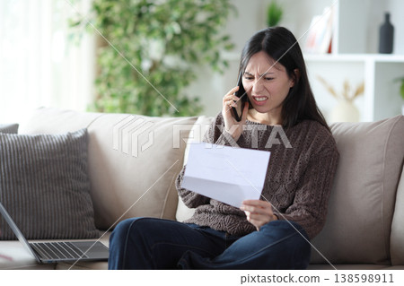 Angry asian woman claiming on phone at home Angry asian woman claiming on phone at home 138598911