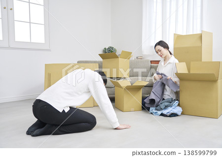 A man bows deeply in apology during a move while a woman packs his belongings. A man bows deeply in apology during a move while a woman packs his belongings. 138599799
