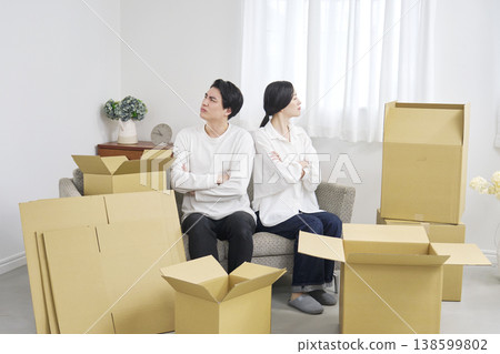 A disgruntled couple stands back-to-back with their arms linked during a move. A disgruntled couple stands back-to-back with their arms linked during a move. 138599802