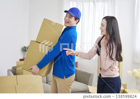 一名搬家公司工人抱著紙箱，一位女士微笑著指導搬家事宜。 138599824