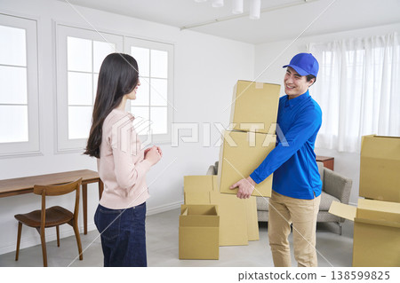 一名搬家公司工人抱著紙箱，一位女士微笑著指導搬家事宜。 138599825