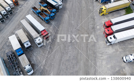 Aerial view of a large truck parking lot at a logistics hub, with multiple commercial semi trucks parked in organized rows. 138600940
