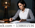 A businesswoman in a white shirt concentrating on reviewing documents in her study at night. 138601536