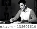A black and white portrait of a man in a white shirt reviewing documents in his study at night. 138601610