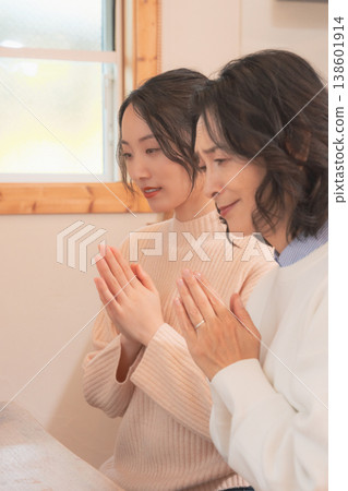 A mother and daughter praying for the deceased at home (retro style) A mother and daughter praying for the deceased at home (retro style) 138601914