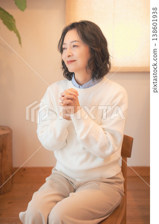 A middle-aged woman (in a retro style) offers prayers for a deceased loved one at home. A middle-aged woman (in a retro style) offers prayers for a deceased loved one at home. 138601938