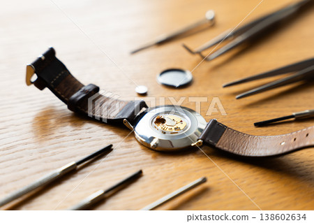 Watch components displayed on a wooden surface, featuring a dismantled wristwatch with leather strap and tools arranged around it 138602634