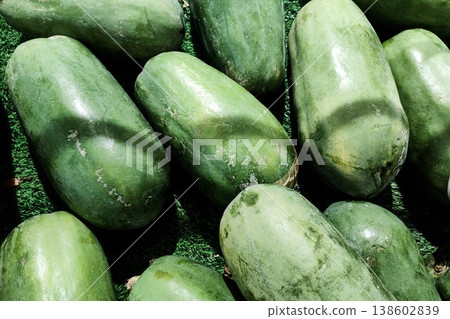 Fresh Green Papayas Laying on a Green Surface at a Market, Displaying Natural Texture and Color, Perfect for Tropical Fruit Imagery Fresh Green Papayas Laying on a Green Surface at a Market, Displaying Natural Texture and Color, Perfect for Tropical Fruit Imagery 138602839