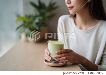 Woman holding matcha latte at wooden table indoors 138602842