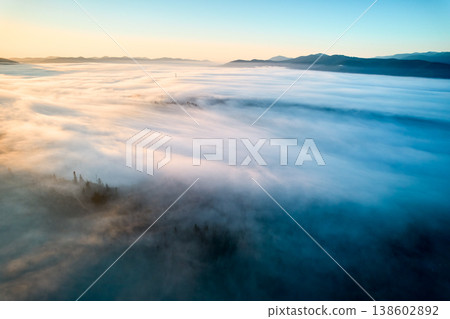 Stunning aerial view of sunrise over mountainous landscape, with thick fog blanketing valleys and hills. Sun's golden rays pierce through mist, casting serene glow over the entire scene. Stunning aerial view of sunrise over mountainous landscape, with thick fog blanketing valleys and hills. Sun's golden rays pierce through mist, casting serene glow over the entire scene. 138602892