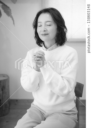 A middle-aged woman prays for a deceased loved one at home (black and white). A middle-aged woman prays for a deceased loved one at home (black and white). 138603148