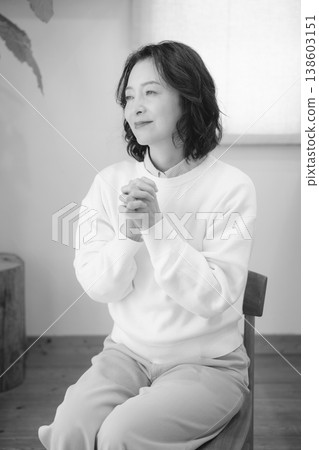 A middle-aged woman prays for a deceased loved one at home (black and white). A middle-aged woman prays for a deceased loved one at home (black and white). 138603151