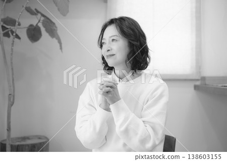 A middle-aged woman prays for a deceased loved one at home (black and white). A middle-aged woman prays for a deceased loved one at home (black and white). 138603155