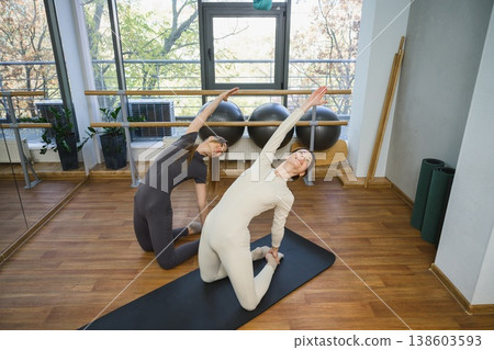 Two women performing synchronized yoga stretch in fitness studio. Two women performing synchronized yoga stretch in fitness studio. 138603593