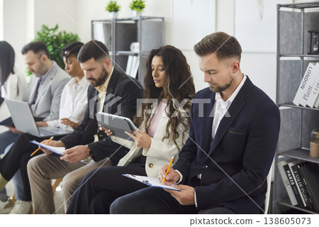Employees working on devices, making notes seated in row in office 138605073