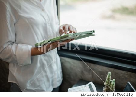 A business professional interacts with a tablet by a window, showcasing modern technology in a minimalist office environment. 138605110