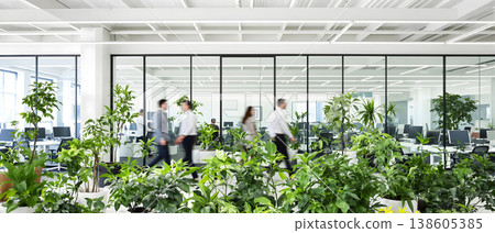 Photo of a modern open office space with indoor plants and blurred people walking, promoting a healthy and productive work environment. 138605385