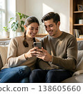 Happy young couple relaxing on the sofa at home, smiling and browsing content on smartphone together. Concept of modern relationships, digital communication and cozy leisure time. 138605660