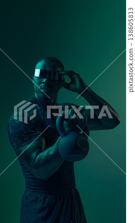 Athlete holding kettlebell and adjusting futuristic visor in neon lighting. Athlete holding kettlebell and adjusting futuristic visor in neon lighting. 138605813