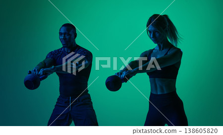 Athletic couple performing kettlebell front raise exercise in neon fitness studio lighting Athletic couple performing kettlebell front raise exercise in neon fitness studio lighting 138605820