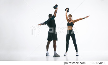 Athletic couple performing rotational kettlebell exercise isolated on white. 138605846
