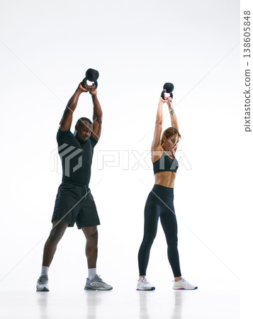 Sport couple lifting kettlebells overhead isolated on white background. 138605848