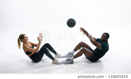 Athletic couple doing sit up exercise with medicine ball isolated on white. Athletic couple doing sit up exercise with medicine ball isolated on white. 138605859