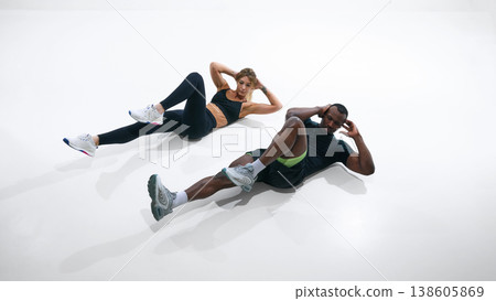Fitness couple doing bicycle crunch exercise isolated on white background. Fitness couple doing bicycle crunch exercise isolated on white background. 138605869