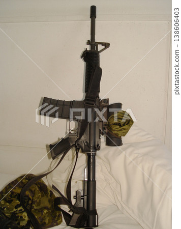 War, camouflage and a rifle on a bed in the home of a soldier ready for conflict, battle or fighting. Army, military or weapon leaning against a wall in an apartment for self defense or patriotism War, camouflage and a rifle on a bed in the home of a soldier ready for conflict, battle or fighting. Army, military or weapon leaning against a wall in an apartment for self defense or patriotism 138606403