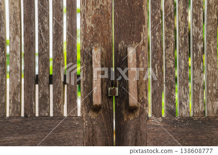 Old wooden gate with metal lock and vertical slats, weathered texture and rustic entrance detail in tropical setting Old wooden gate with metal lock and vertical slats, weathered texture and rustic entrance detail in tropical setting 138608777